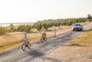 Kolm jalgratturit sõidavad auto ees.