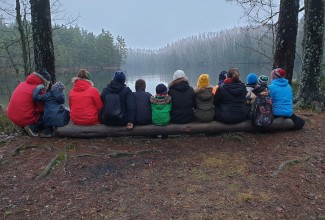 Puhkepaus metsarajal, kõik inimesed istuvad pingil seljaga pildistaja poole.